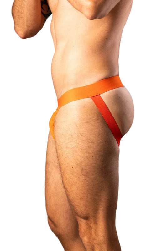 A close-up side view of a male model wearing bright orange and red athletic tape or a very minimal brief-style support garment against a blue studio background.