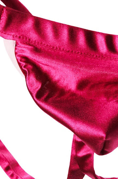 A hot pink satin thong with adjustable straps and a small metal ring at the back, displayed against a solid white background.