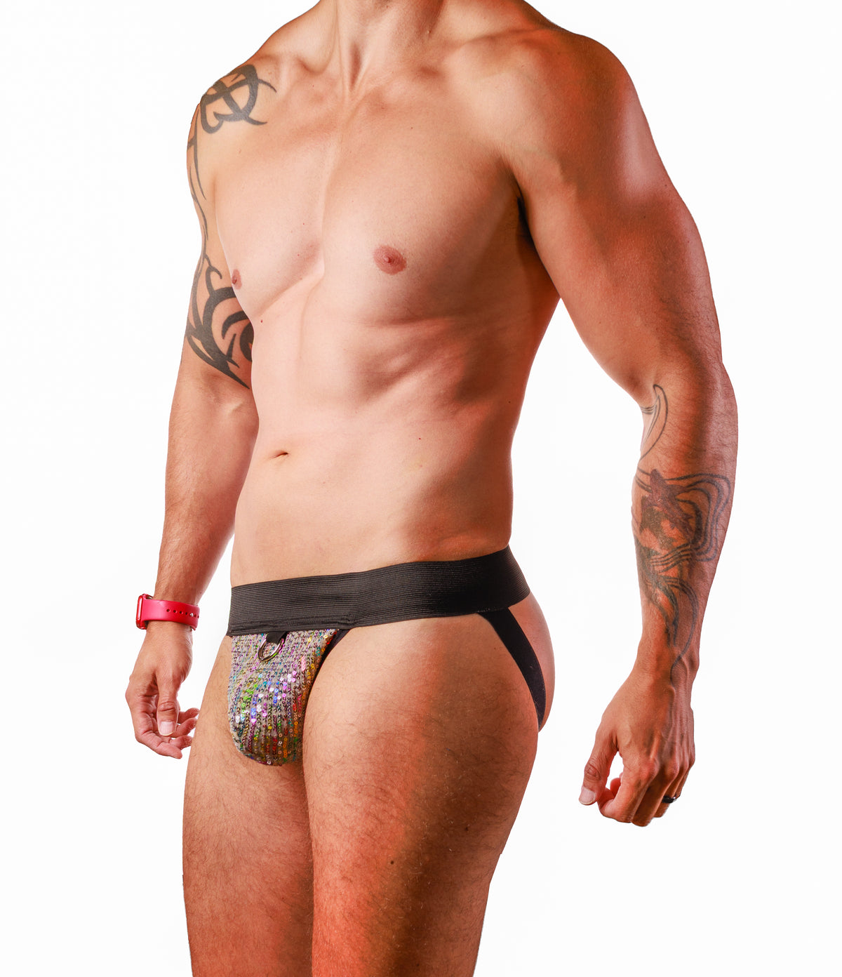 A shirtless male model wearing a low-rise, asymmetrical men's brief. The front panel is covered in a dense, iridescent sequin pattern that shifts colors, while the waistband and side straps are solid black.