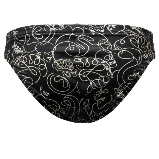 Black swim briefs featuring an all-over white continuous line art pattern of skulls, snakes, and abstract doodles, shown against a plain white background.