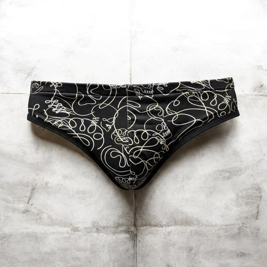 Black bikini-style underwear with an abstract white line pattern, laid flat on a light gray tiled surface.
