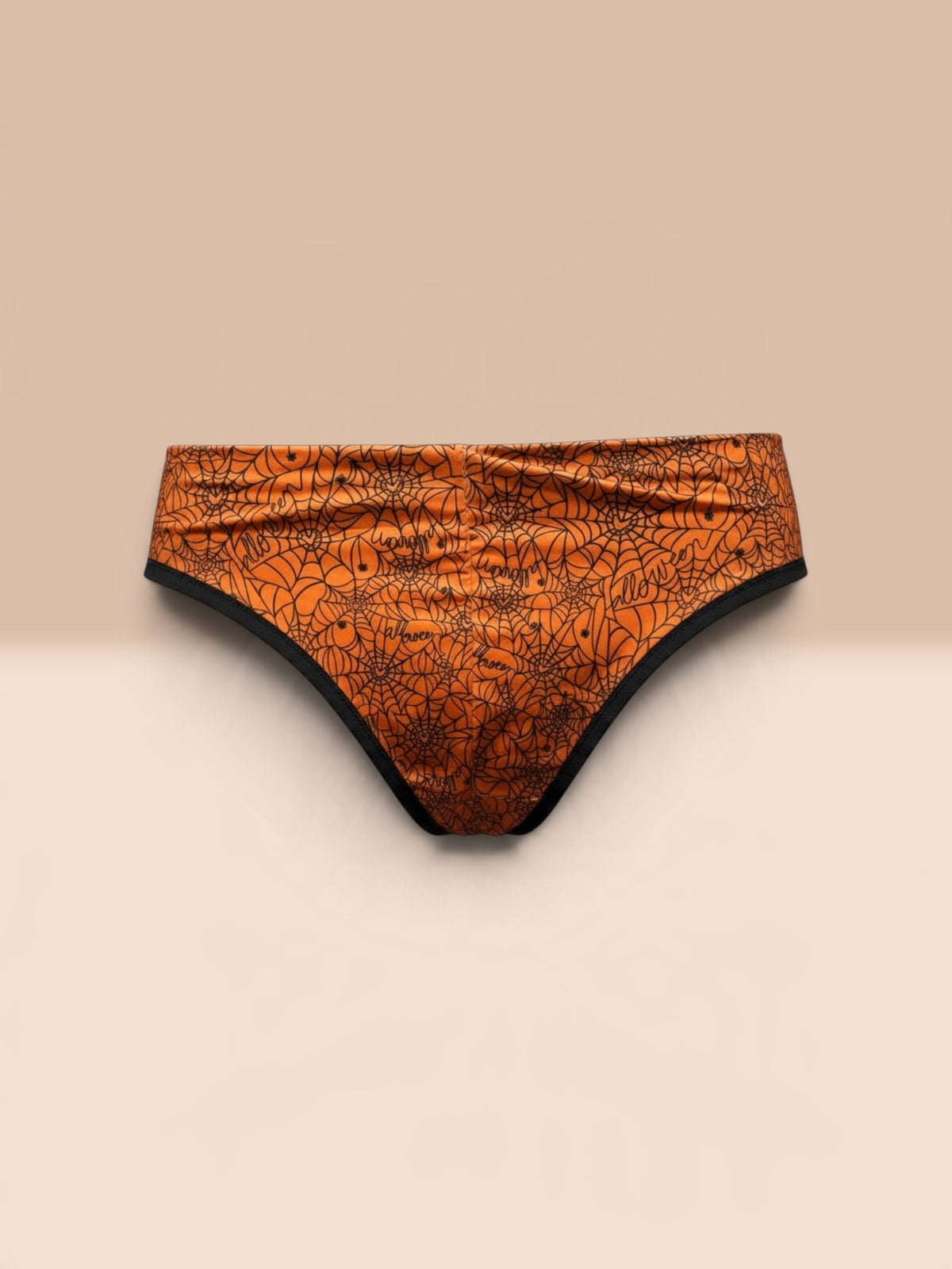 Orange bikini bottoms with a black spiderweb and spider graphic print, displayed on a light wooden surface against a dark gray background.